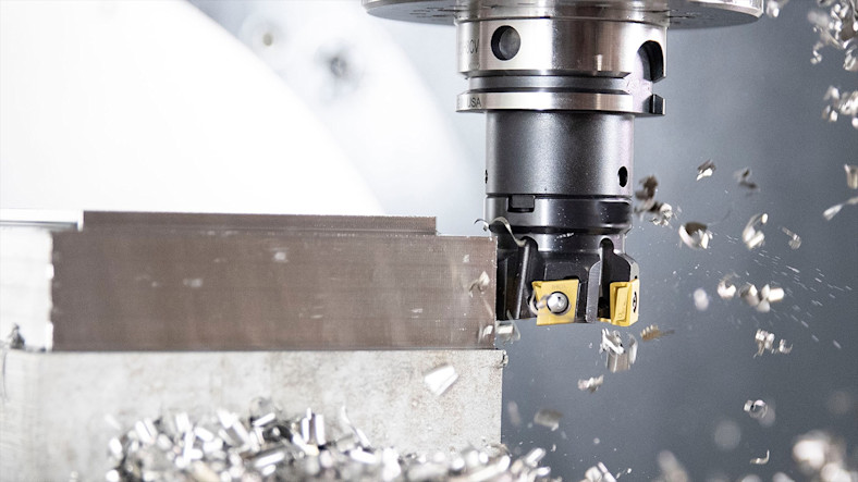 Close-up of a Kennametal milling cutter cutting into metal, with shards flying.