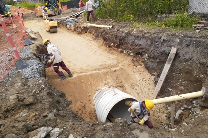Construction workers attend to a large water pipe buried underground.