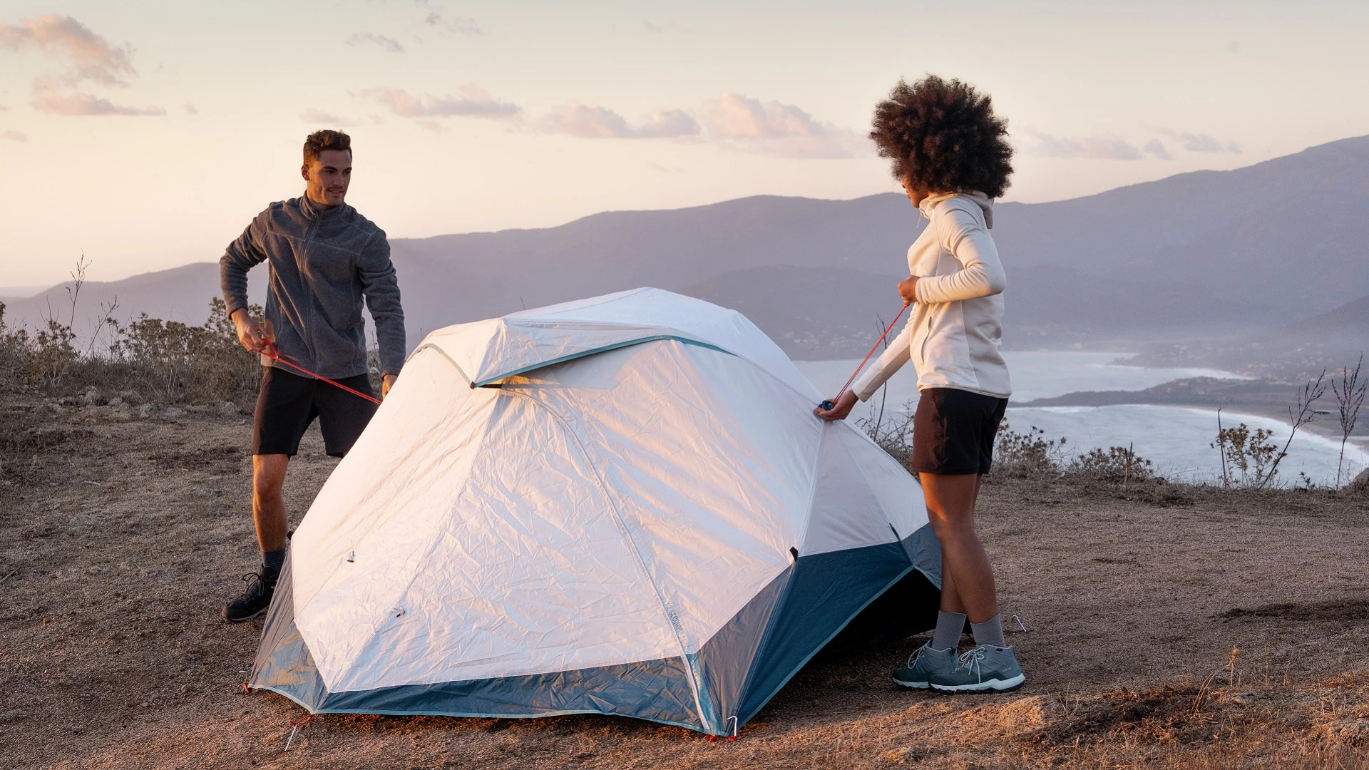 两个人在俯瞰湖泊的悬崖上搭起了露营帐篷。