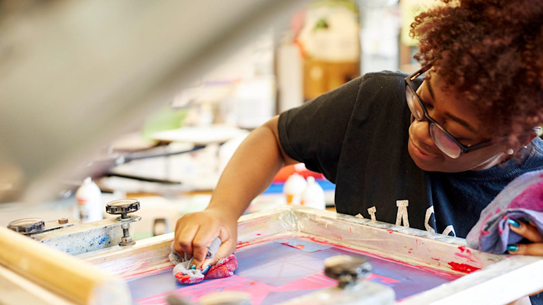 A young woman removes ink from a screen-printing screen. 