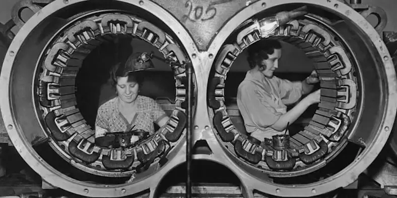 Black and white photo of women working on airplane manufacturing WWII