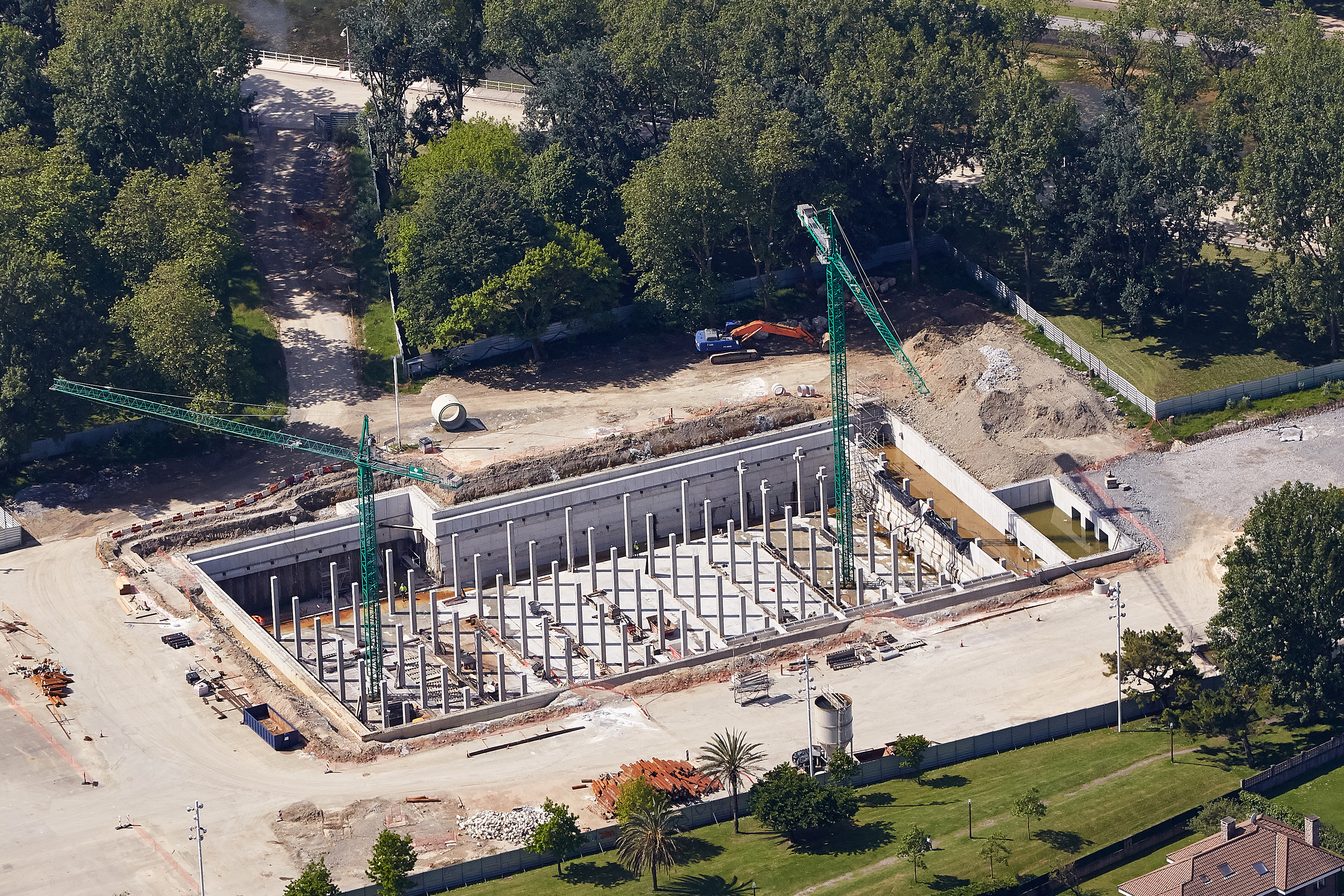 Aerial view of the Hermanos Castro storm tank under construction in Gijón, showing the reinforced concrete structure, internal support columns, and ongoing civil engineering works.