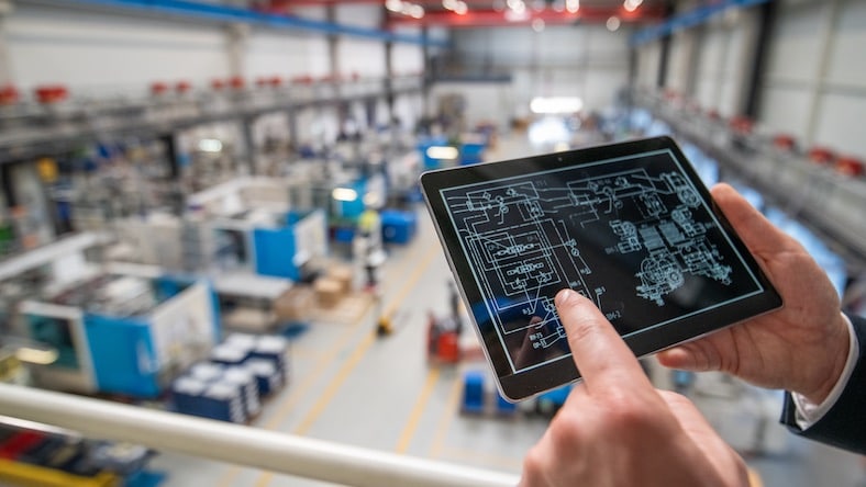 Close-up of hand holding digital tablet showing factory schematics