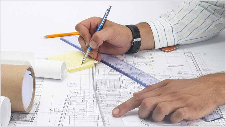 Hands work on an architectural blueprint with a ruler and pen.