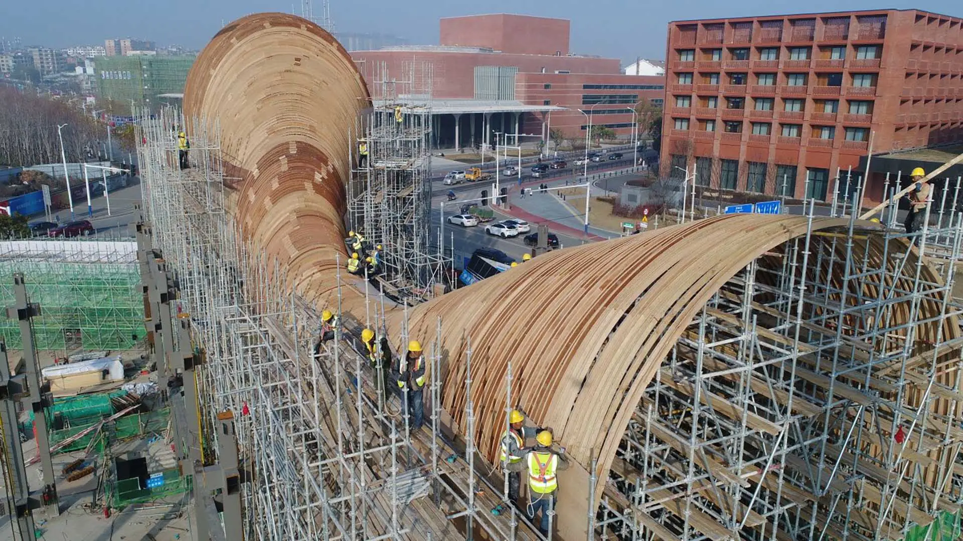 Construction workers on scaffolding work on a large curved wooden building structure.