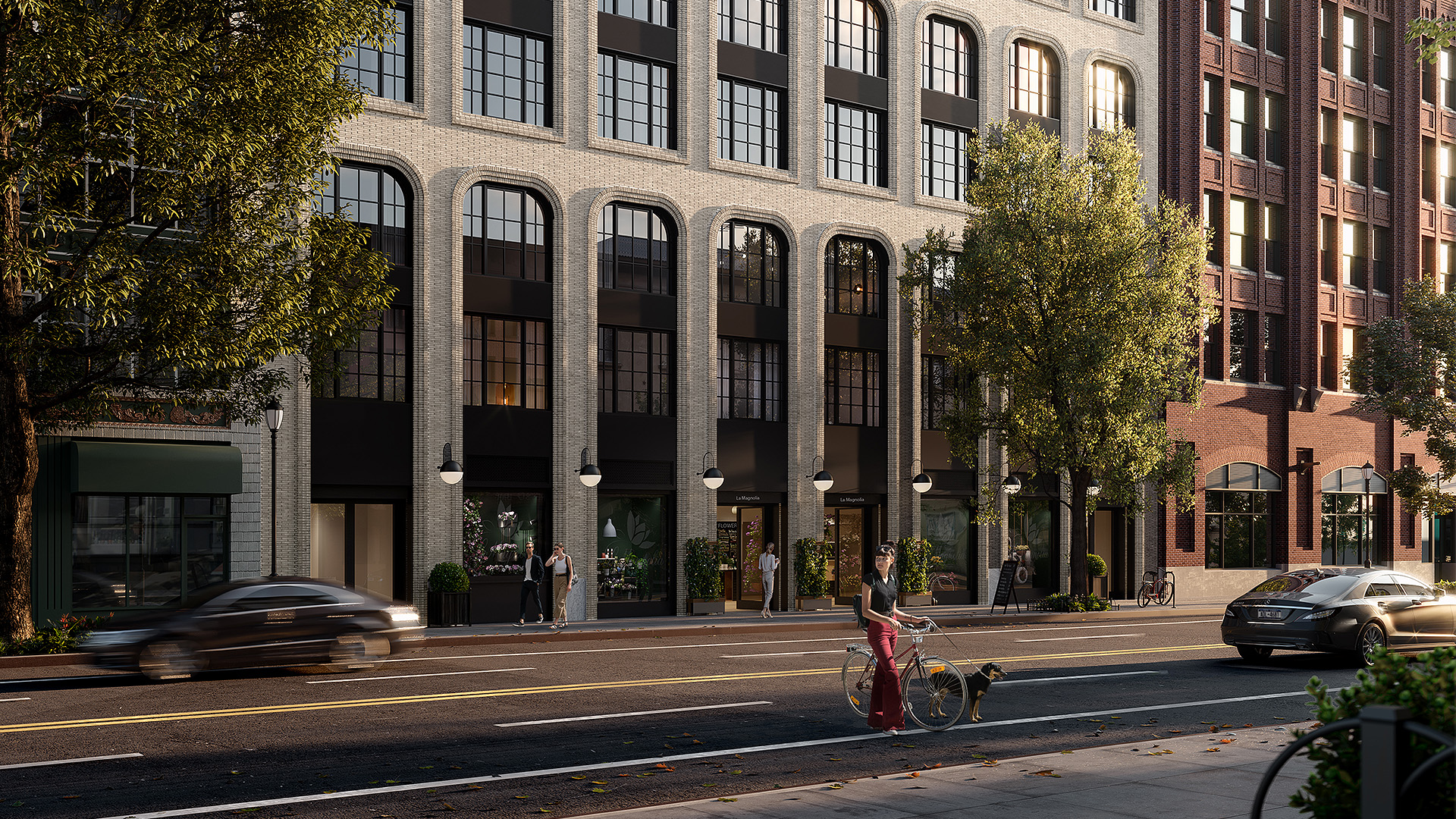 Modern brick buildings with large arched windows, trees, bicycles parked, and a busy street with cars driving by.