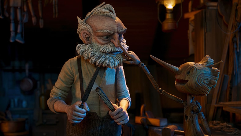 A still from the stop-motion animated film Guillermo del Toro’s Pinocchio shows the wooden marionette Pinocchio smiling and touching the nose of the old man woodcarver Geppetto.