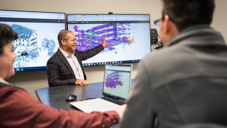 A man stands in front of a software screen displaying a building model