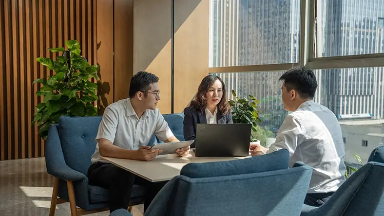 Business meeting with three professionals discussing work at a modern office table.
