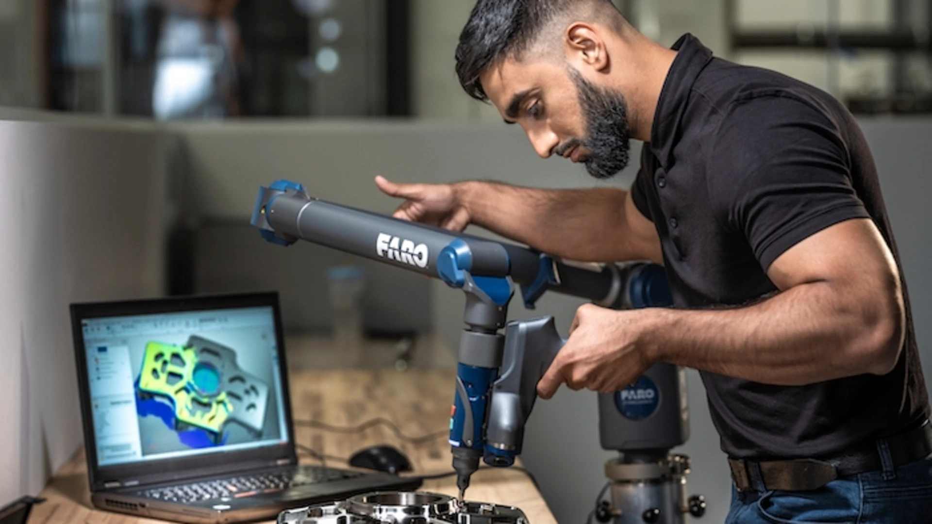 a person using a machine to work on a part in front of a laptop