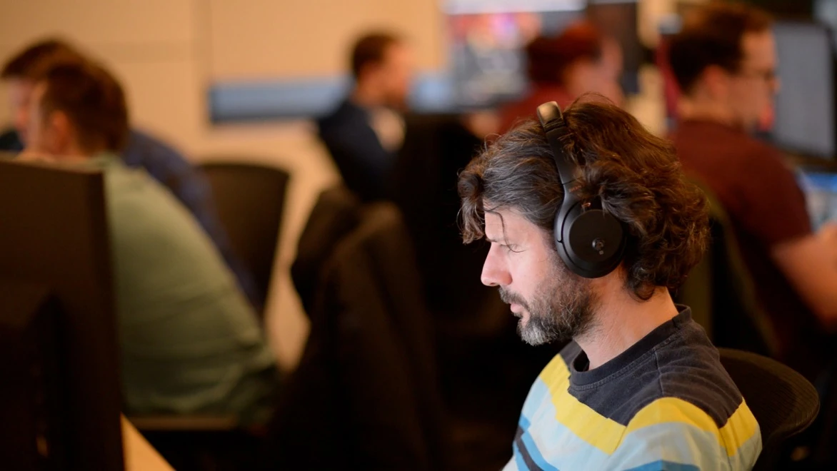 A white male artist with a beard and wearing headphones concentrates on a computer screen.