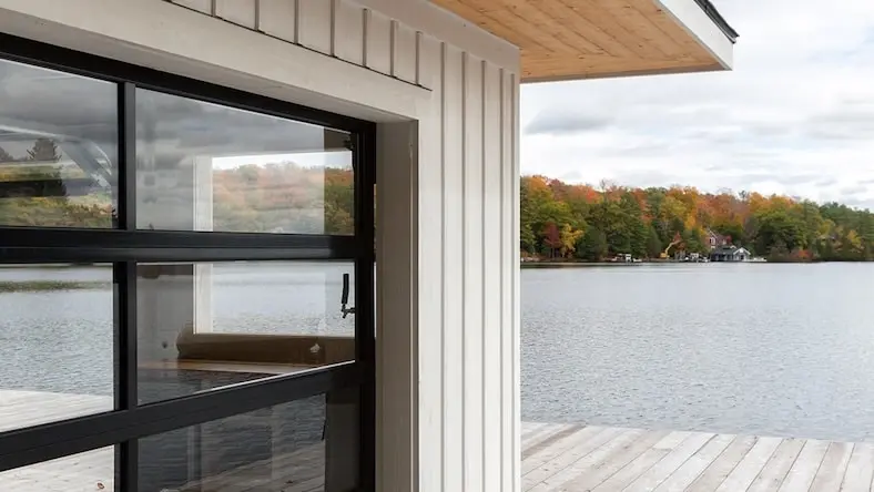 A modern home with large windows overlooks a lake and trees.