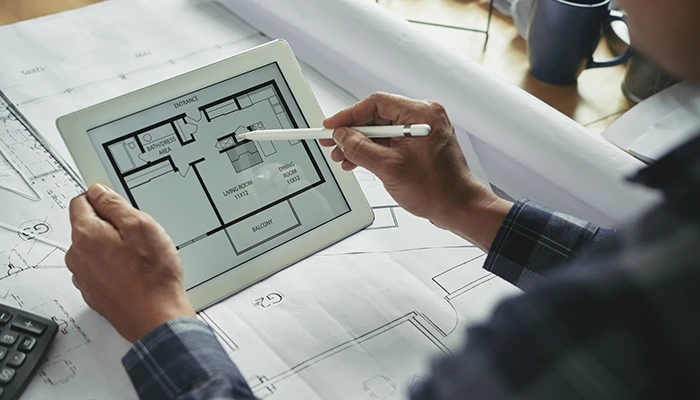 An architect uses a stylus on a tablet showing a room layout