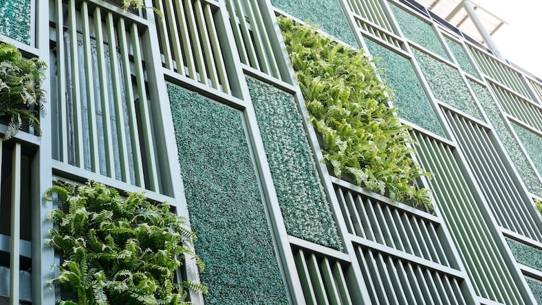 A building is clad in a green facade featuring plant-filled panels.