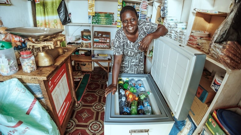 A smiling Ugandan show owner proudly displays the products in her solar-powered EasyFreeze100 freezer.