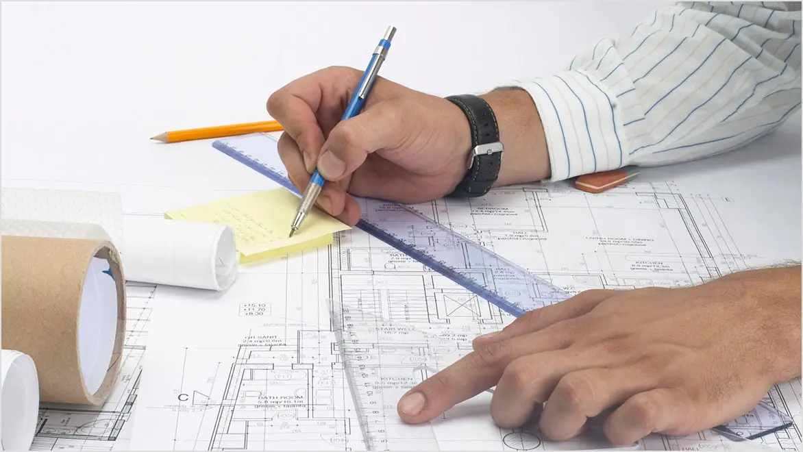 Two hands drawing a floor plan on paper with a pen, sticky notes, and ruler.