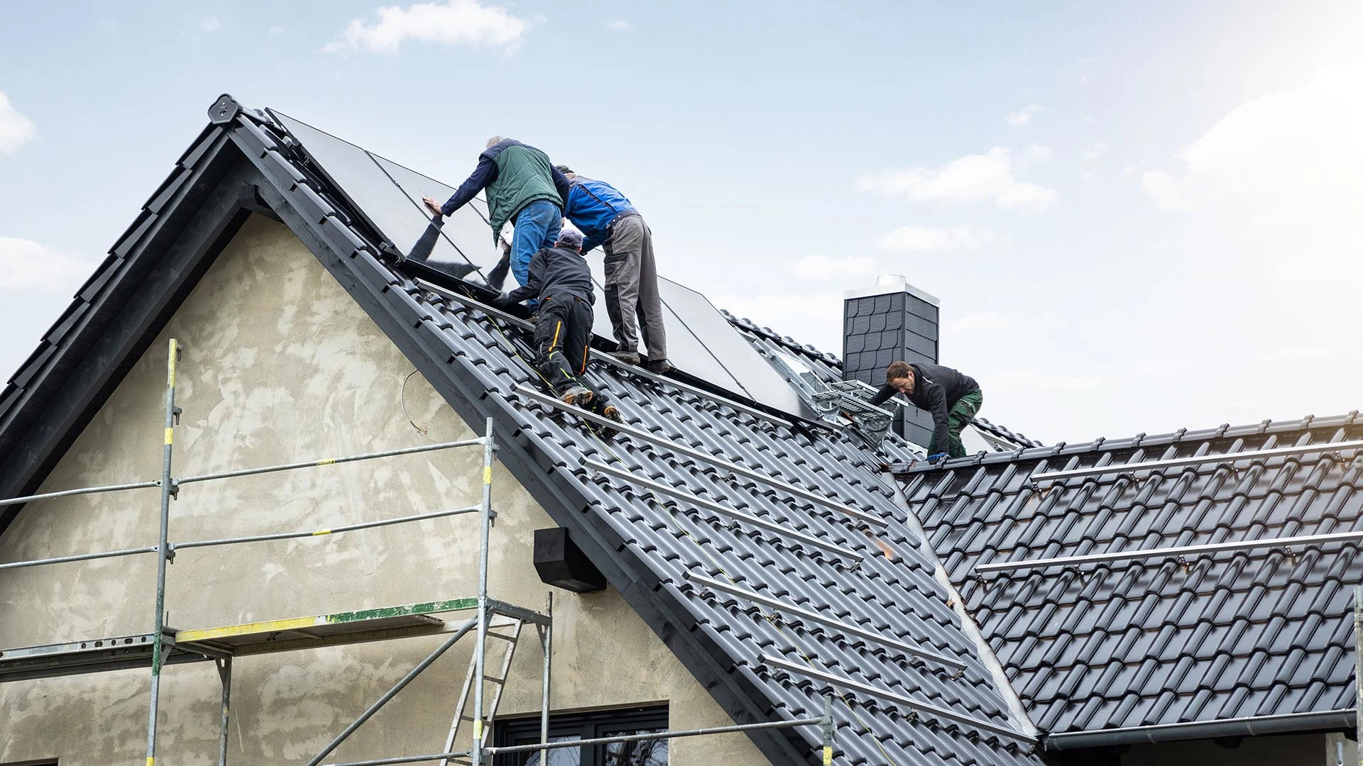 A team of four workers is installing photovoltaic modules on the roof of a building.
