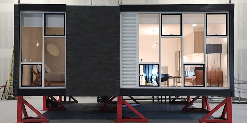 An assembled modular apartment unit sits on supports inside a production facility