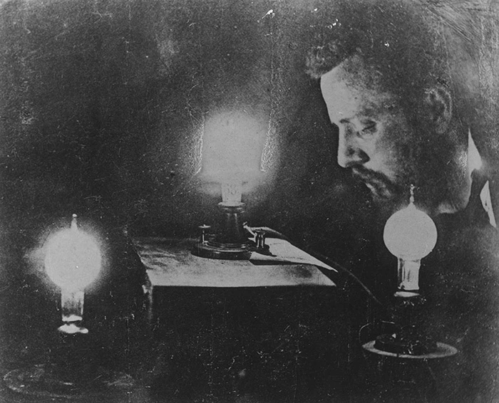 Grainy black and white photo of Charles Batchelor in profile with light bulbs