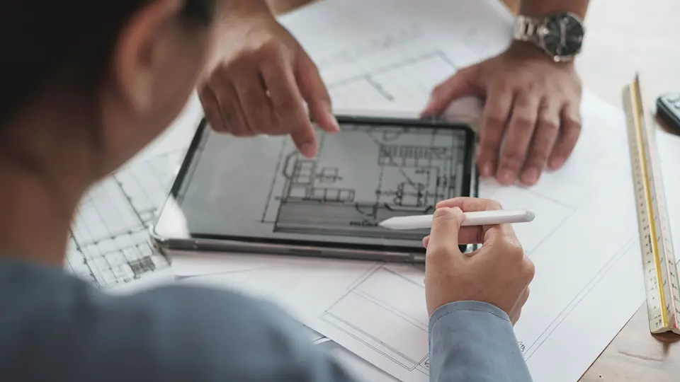 Designers consult a tablet screen displaying room blueprints.