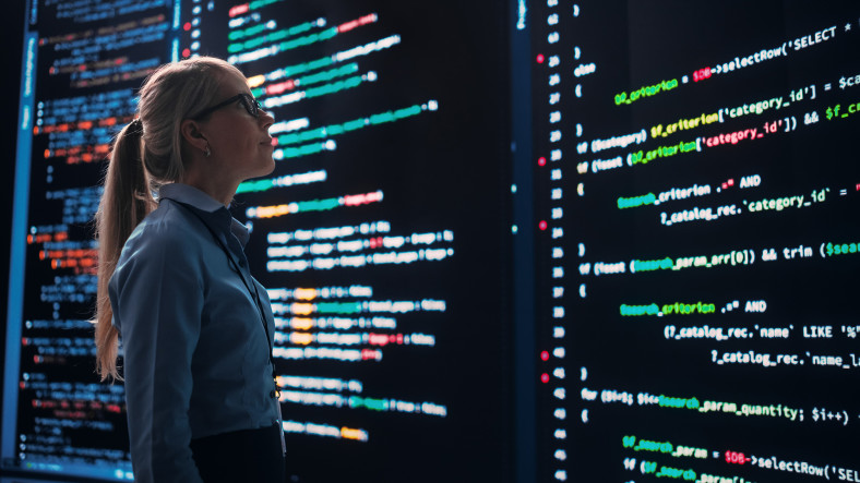 A woman analyzes lines of code displayed on large screens.