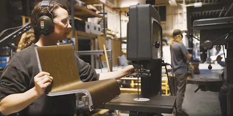 A person wearing hearing protection ear muffs holding an object close to a drill.