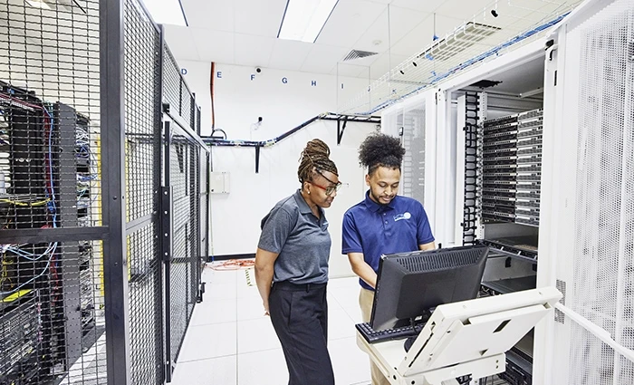 Two IT workers look at monitor in a server room.
