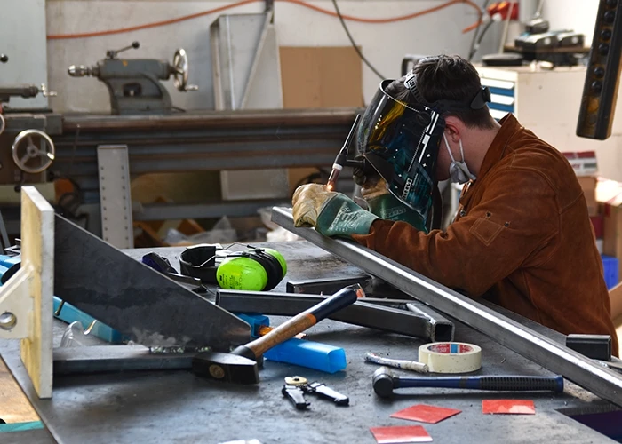 A student wears a welding mask in a workshop.