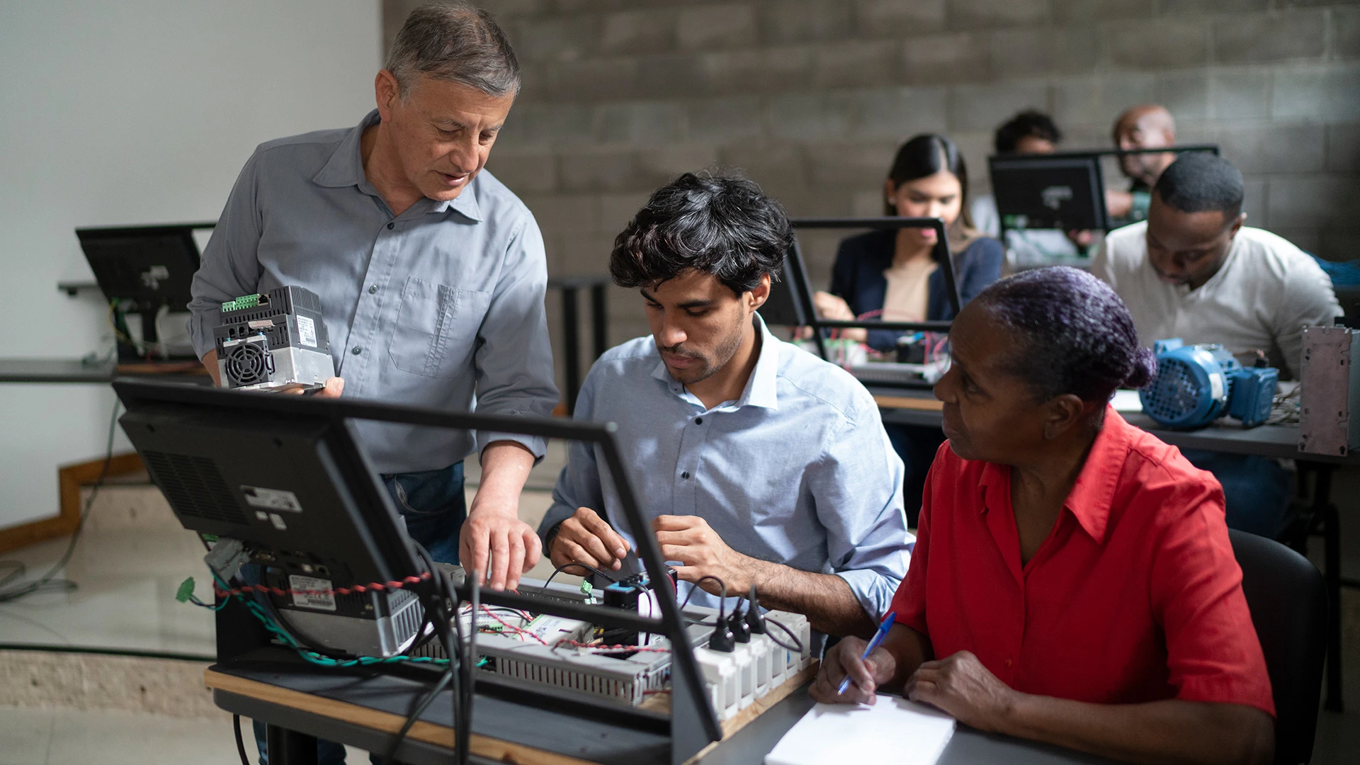 Un profesor de electrónica da explicaciones a un grupo de estudiantes adultos en un aula.