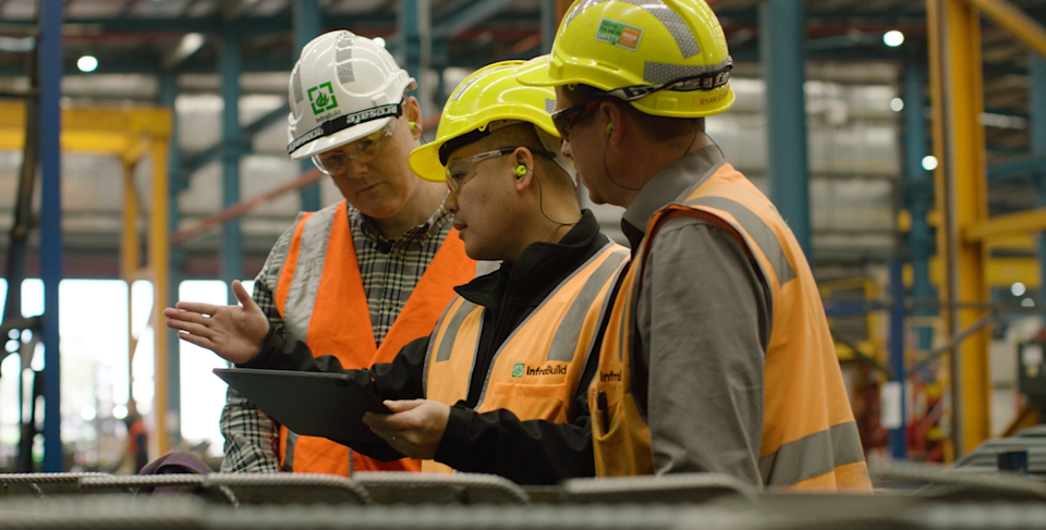 Three InfraBuild employees on factory site, looking at site designs on a tablet.