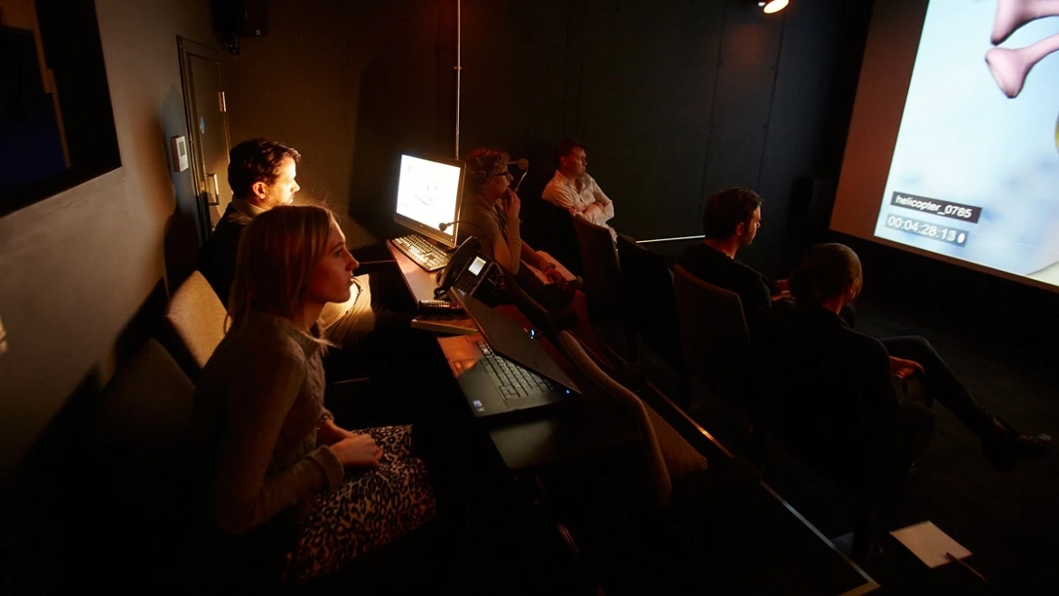 Visual effects artists review their work on a large screen in a darkened screening room.