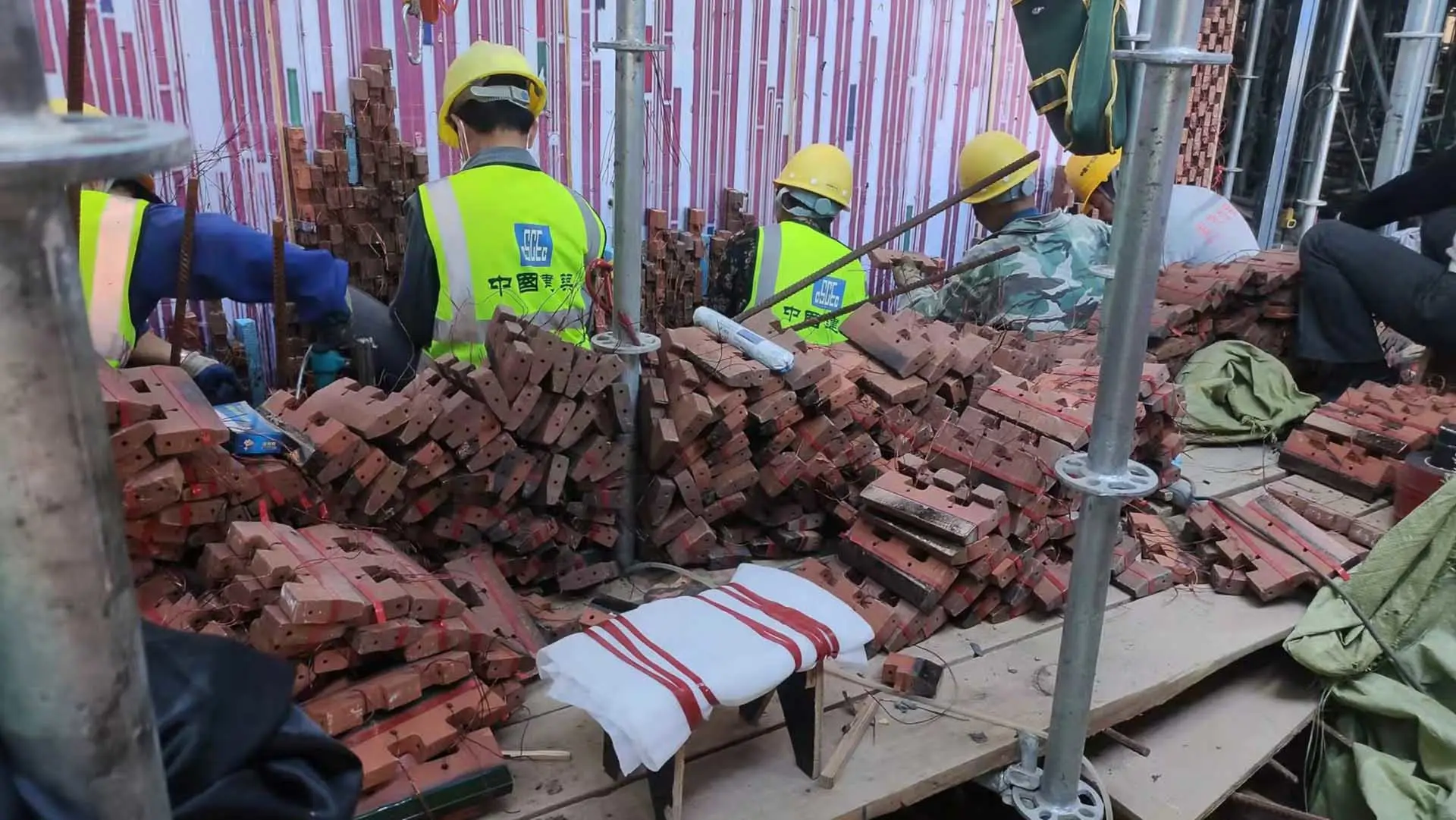 Workers in safety vests handle piles of ceramic tiles at a construction site.