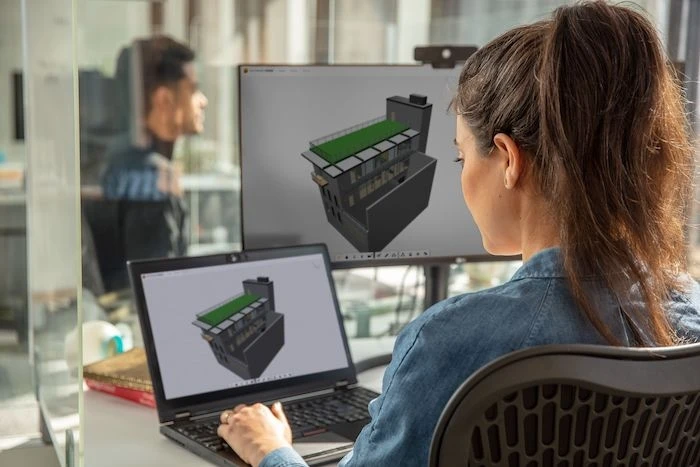 Digital factoryA woman in a ponytail sits at a desk with a laptop and an external monitor showing the same rendering.