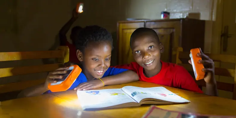 Two children reading a book using a handheld light.