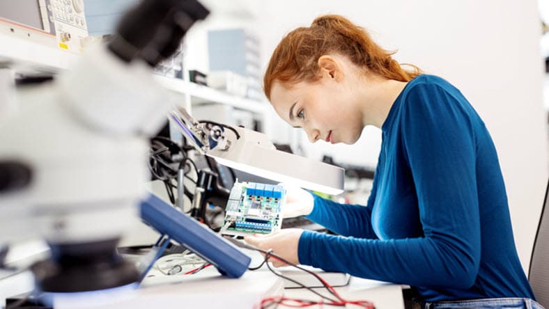A female electrical engineering student tests a prototype circuit board using a virtual simulation during a class in the technology lab