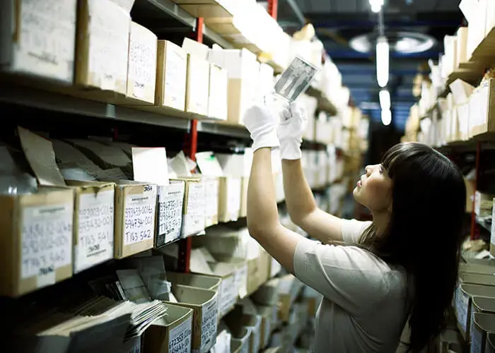 A person in between two rows of boxes and files, holding up a photo negative to the light.