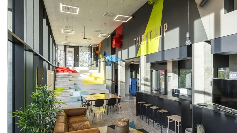 A colorful modern office space has large windows, green plants, and multiple collaboration spaces.