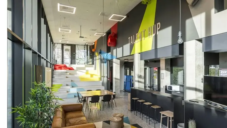 A colorful modern office space has large windows, green plants, and multiple collaboration spaces.