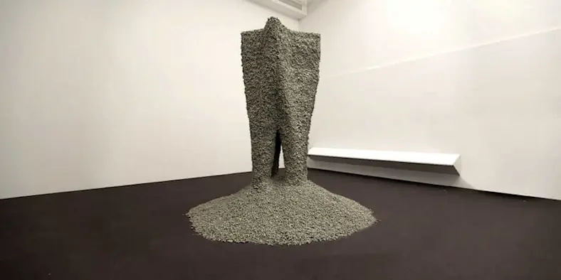 A large sculptural form, composed of small rocks held together with string, in a gallery setting. 