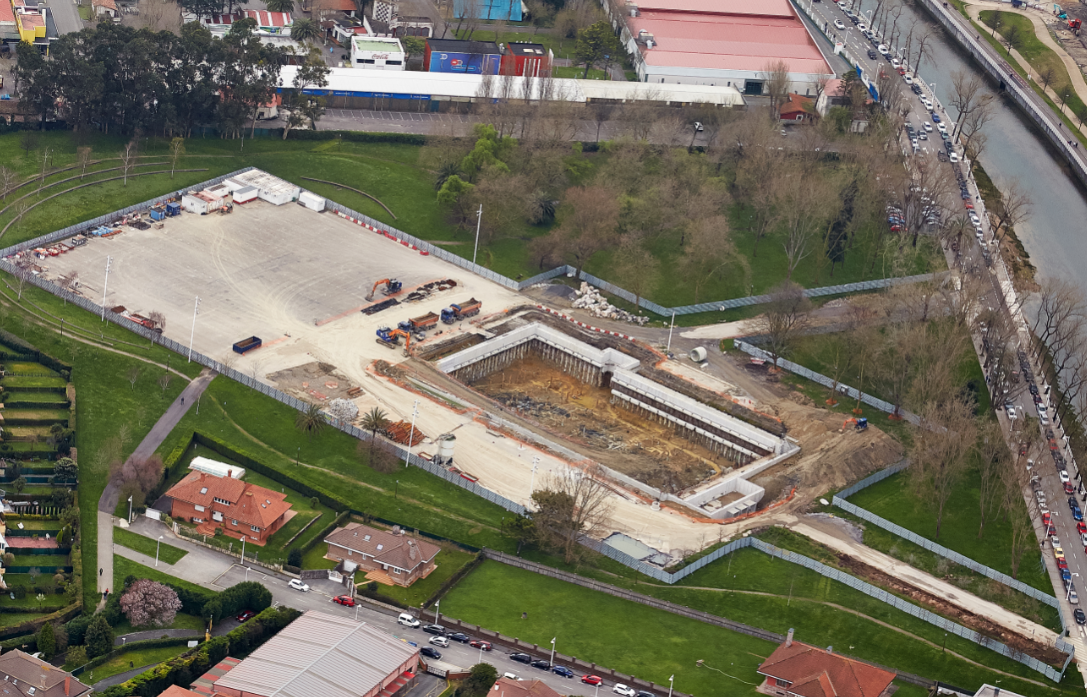 Vista aérea del tanque de tormentas Hermanos Castro en construcción en Gijón, mostrando la zona de excavación dentro de un parque urbano y la infraestructura de drenaje circundante.