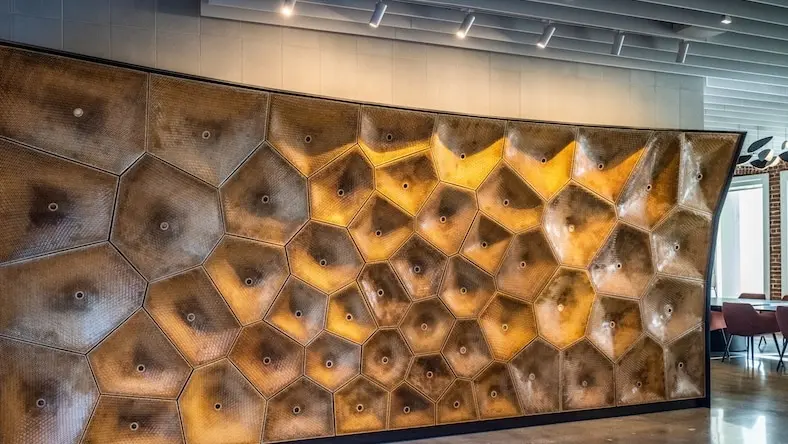 A large wood sculpture on the wall of an office building is illuminated by track lighting.