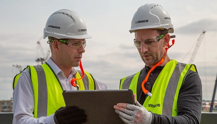 Two construction workers check data on a tablet.