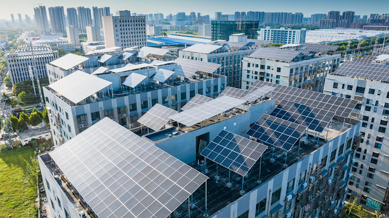 Solar panels cover the rooftops of multiple buildings as a dense cityscape stretches into the background.  