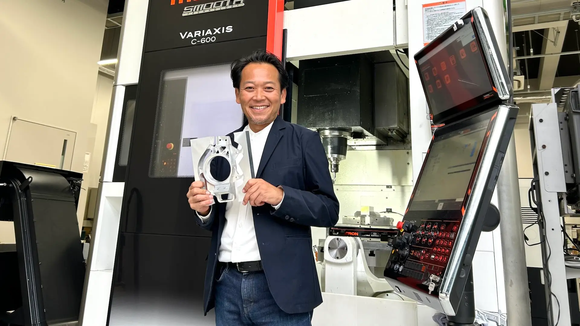 Professor Hiroto Hamane, director of the Manufacturing Support Center at Kogakuin University, stands in front of a CNC machine in the 5-axis machining center on the Hachioji Campus.