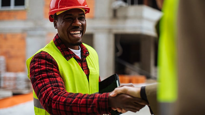 A man shakes his client's hand on a construction site.