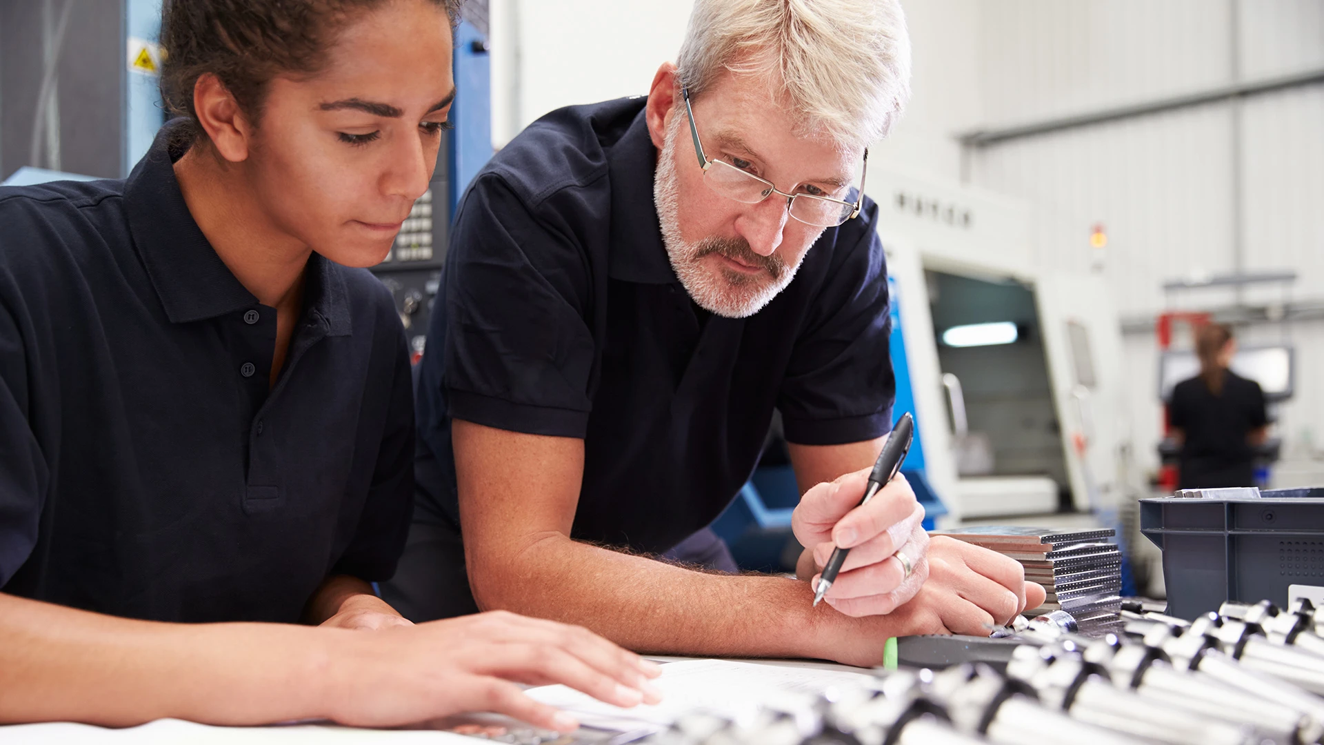 Engineer and apprentice making notes and calculations to plan a CNC machining project