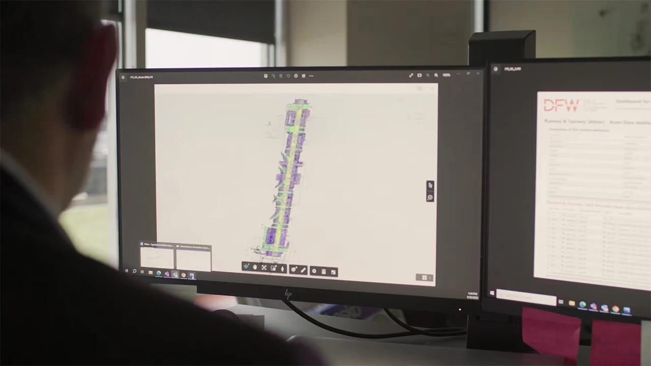 Person reviews a detailed digital site plan displayed across dual computer monitors in an office workspace.