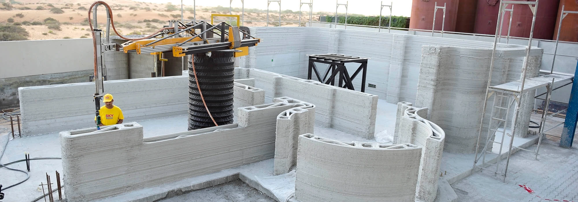 A construction worker observes a concrete printer fabricate wall structures