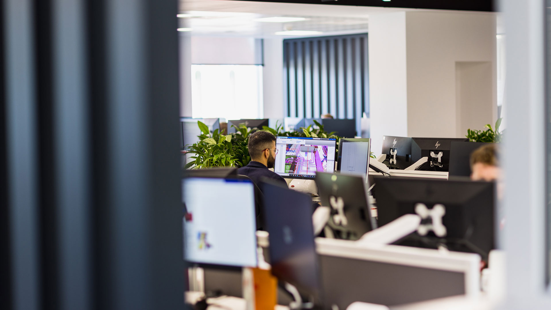 A man sits in front of dual monitors in an open-office setting