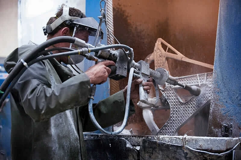 Worker sandblasts residue from a metal airplane seat frame.